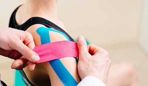 Therapist applying kinesiology tape on shoulder.